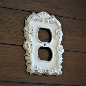 May include: White porcelain outlet cover with a decorative floral design. The cover has a distressed finish and is designed to look vintage.