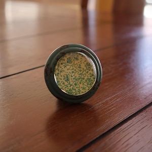 Pode incluir: Um botão de armário de cerâmica azul-esverdeado e branco com acabamento desgastado.