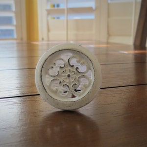 May include: White decorative cabinet knob with a detailed floral design. The knob is round and has a raised edge.