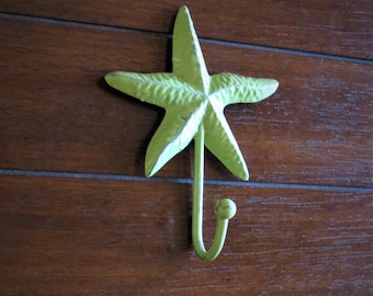 Può includere: Un gancio a forma di stella marina in metallo verde montato su una parete di legno.