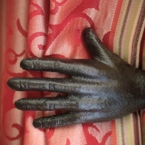 May include: A black cast iron hand resting on a red and white patterned fabric. The fabric has a striped pattern on the bottom.