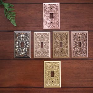 Peut inclure: Un ensemble de dix plaques de prise décoratives en différentes finitions, dont le cuivre, le laiton et le nickel. Chaque plaque présente un motif floral complexe.