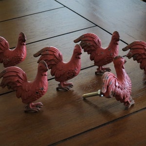 May include: Six red rooster-shaped drawer pulls with a rustic finish. The pulls are made of metal and have a detailed design.