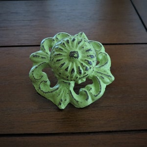 Op de afbeelding: Een groene gietijzeren ladetrekker met een bloemmotief. De trekker heeft een verweerde afwerking en een verhoogd midden.