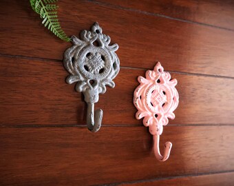 May include: Two decorative hooks with ornate designs. One hook is silver and the other is pink.