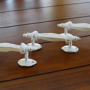 Pode incluir: Quatro puxadores de gaveta de ferro fundido branco com acabamento desgastado. Cada puxador tem um design decorativo torcido em cada extremidade.