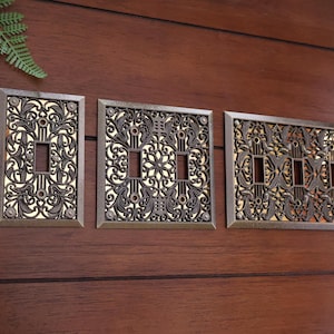 May include: Three decorative light switch covers with an ornate, filigree design. The covers are made of metal and have a gold finish.