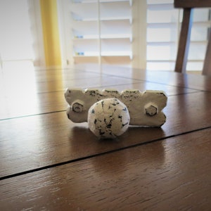 May include: White cast iron cabinet knob with a round, distressed finish. The knob is attached to a rectangular base with two screw holes.