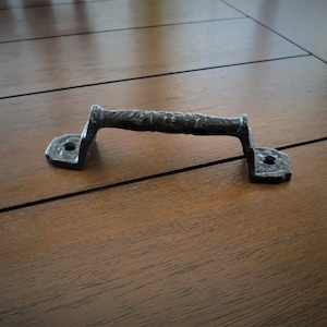 May include: Black metal door handle with a textured design. The handle is on a wooden surface.