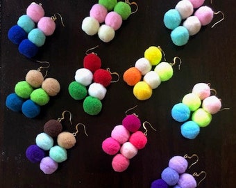 May include: Assortment of colorful pom-pom earrings. Each pair features three pom-poms in different colors, including red, blue, green, yellow, pink, and purple.