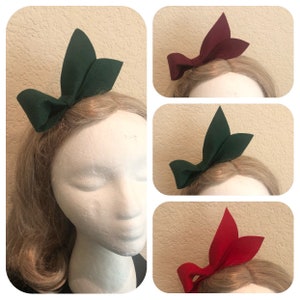 May include: Three felt hair bows in different colours: green, burgundy and red. Each bow is tied in a simple knot and has a pointed shape.
