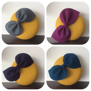 May include: Four felt hats with a yellow base and a large bow on top. The bows are in different colours: grey, purple, navy blue, and teal.