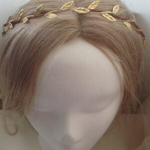 May include: A gold leaf crown headband with brown wire. The headband is on a white mannequin head with blonde hair.