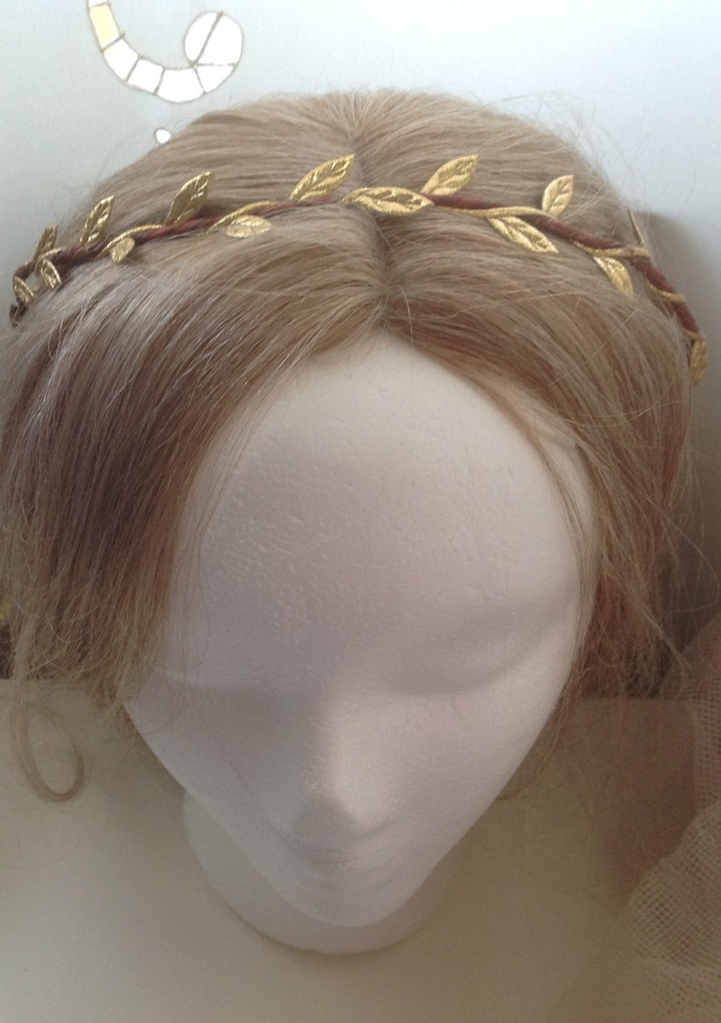 May include: A gold leaf crown headband with brown wire. The headband is on a white mannequin head with blonde hair.
