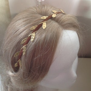 May include: A brown headband with gold leaf accents. The headband is worn on a mannequin with blonde hair.