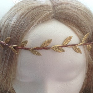 May include: A gold leaf crown with a brown wire base. The crown is worn on a mannequin head with blonde hair.
