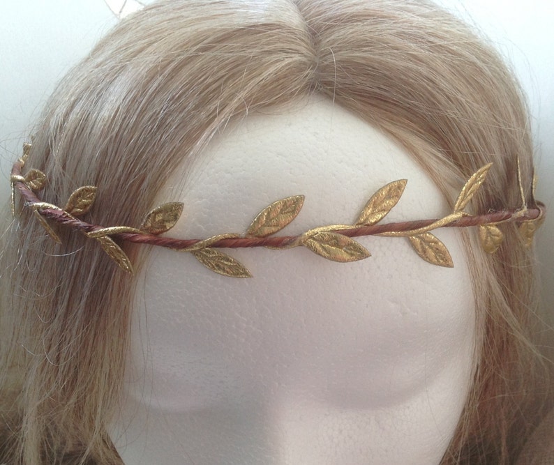 May include: A gold leaf crown with a brown wire base. The crown is worn on a mannequin head with blonde hair.