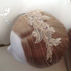 May include: A delicate ivory lace headband with pearl accents. The headband is adorned with a floral design and is perfect for adding a touch of elegance to any hairstyle.