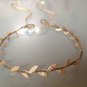 May include: A gold leaf headband with a delicate, twisted wire base. The leaves are arranged in a circular pattern, creating a crown-like effect.