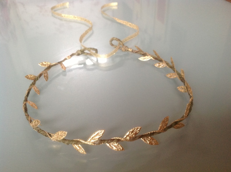 May include: A gold leaf headband with a delicate, twisted wire base. The leaves are arranged in a circular pattern, creating a crown-like effect.