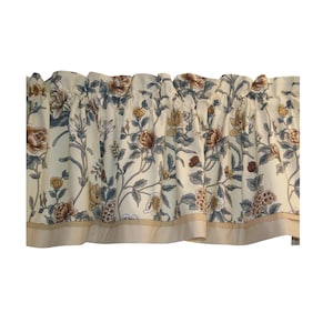 May include: A window valance featuring a cream-colored background with a floral pattern in shades of brown, yellow, and muted blue. The fabric has a gathered top for rod insertion and a solid tan border along the bottom edge with a subtle dot texture.