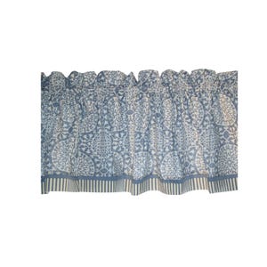 May include: A blue and white window valance featuring a repeating circular medallion pattern across the main body, finished with a gathered top header and a bottom border consisting of vertical stripes in coordinating blue and white tones.