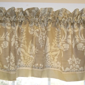 Peut inclure: Une cantonnière beige avec un motif floral blanc. La cantonnière a un haut plissé et une bordure inférieure unie.
