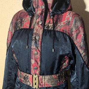 May include: A black ski suit with a red, gold and black patterned design. The suit has a hood and a belt with a gold buckle.