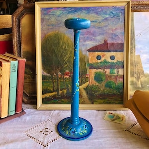 May include: A tall, blue wooden hat stand featuring a rounded top, a slender cylindrical stem, and a circular base. The stand is decorated with hand-painted green leaves and small blue flowers along the stem and around the base perimeter.