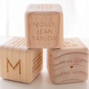 May include: Three wooden blocks with engraved text. The top block reads "Molly Jean Taylor". The middle block has the letter "M" and the bottom block reads "09-03-2027 3.5KG. 50CM".