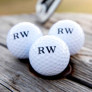 May include: Three white golf balls with the letters "RW" printed in black on each ball.