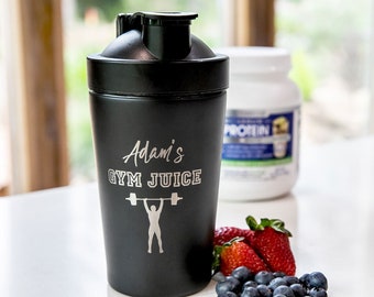 May include: Black insulated tumbler with the text "Adam's GYM JUICE" and a weightlifter graphic. The tumbler is next to a container of protein powder, strawberries, and blueberries.