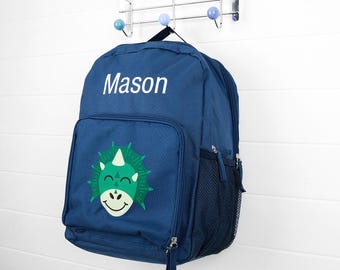 May include: A navy blue backpack with the name "Mason" in white lettering. The front pocket features a green and white dinosaur graphic. The backpack has a black mesh side pocket and a zipper closure.