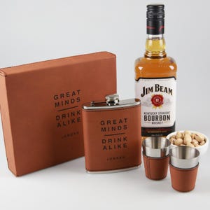 May include: A gift set with a brown leather-covered hip flask and shot glasses, a bottle of Jim Beam bourbon, and a box. The flask and box are embossed with the text "GREAT MINDS DRINK ALIKE JORDAN". A small bowl of pistachios is also included.