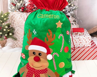 May include: A green Christmas gift bag with a red drawstring closure and top. The bag features a reindeer design with a red hat and scarf, a Christmas tree, and the name "Cameron" embroidered in gold. Festive holiday decor.