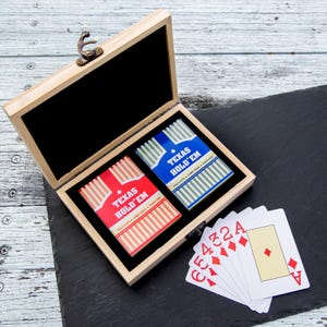 May include: A wooden box with a hinged lid, containing two decks of playing cards labelled "Texas Hold 'Em". One deck is red, the other blue. Five playing cards are fanned out to the side, showing the 5, 4, 3, 2, and Ace of diamonds.
