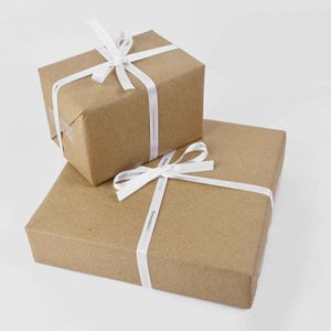 May include: Two brown cardboard gift boxes, one stacked on top of the other. Each box is wrapped with a white ribbon tied in a bow. The ribbon has the word "Personalized" printed on it.