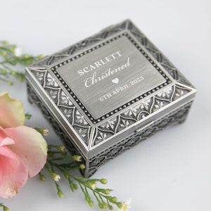 May include: A silver metal keepsake box with an ornate design. The lid is engraved with the text "SCARLETT Christened 6TH APRIL 2025" and a small heart.