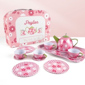 May include: A pink floral tea set with a matching case. The set includes a teapot, cups, saucers, and plates. The case features the name "Peyton" and the text "My First Tea Set". The set is designed for children.