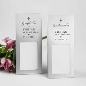 May include: Two silver picture frames with a cross and the words "Godfather to Tobias Elias Alafouzos 11-05-2025" and "Godmother to Tobias Elias Alafouzos 11-05-2025" on them.