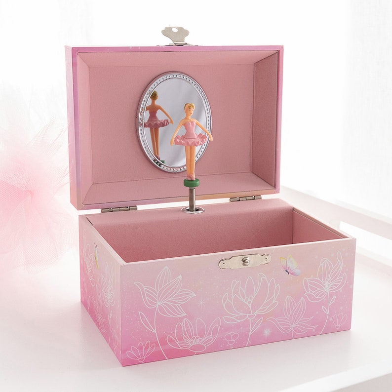 May include: A pink musical jewelry box with a ballerina figurine. The box is decorated with floral designs and a butterfly. Inside, a mirror reflects the ballerina. The box is open, revealing its interior.