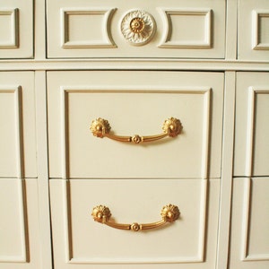 May include: White dresser with gold trim and ornate hardware. The dresser has six drawers with gold handles and a gold trim around the bottom.