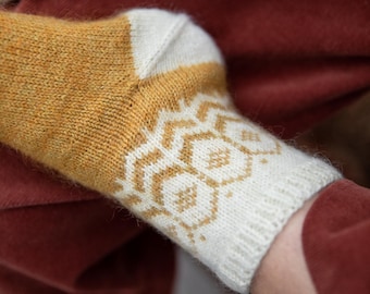 Peut inclure: Gros plan sur une chaussette tricotée avec un motif géométrique. La chaussette présente une palette de couleurs jaune moutarde et crème, avec un motif répétitif sur le bord. La chaussette est faite d'un fil doux et texturé.