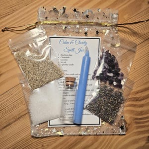 May include: A clear, star-patterned pouch containing a "Calm & Clarity Spell Jar" kit. The kit includes a blue candle, amethyst chips, chamomile, lavender, sea salt, and a small glass bottle. The text on the card lists the contents.