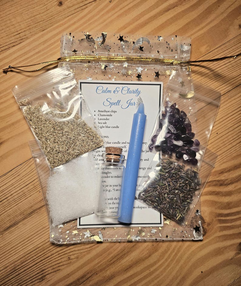 May include: A clear, star-patterned pouch containing a "Calm & Clarity Spell Jar" kit. The kit includes a blue candle, amethyst chips, chamomile, lavender, sea salt, and a small glass bottle. The text on the card lists the contents.