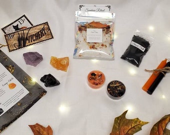May include: A collection of spiritual items including crystals, candles, and ritual supplies. The image features a black mesh bag with crystals, small candles, and a bag of black salt. Decorative fall leaves are scattered around the items.
