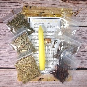 May include: A spell jar kit with a yellow chime candle, small glass bottle, and various herbs in clear plastic bags. The kit includes a list of ingredients and instructions. The text on the label reads "Clear the Path Spell Jar."