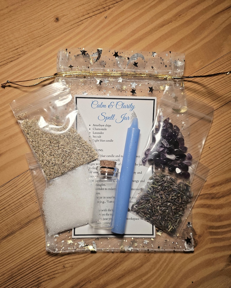 May include: A clear, star-printed bag containing a spell jar kit. The kit includes a blue candle, amethyst chips, chamomile, lavender, sea salt, and a small glass bottle. The label reads "Calm & Clarity Spell Jar."