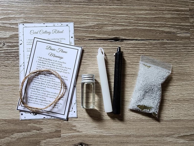 May include: A white candle, a black candle, a small bottle of clear liquid, a bag of white crystals, and two pieces of paper with instructions for a card cutting ritual and basic flame meanings.
