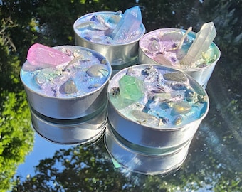 May include: Four tealight candles with embedded crystals. Each candle has a different color crystal: pink, blue, green, and clear. The candles are in silver containers.